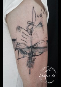 tatouage de bras graphique d'un livre ouvert vieux grimmoire d'où s'envolent des lettres avec une trame dot work pointillisme